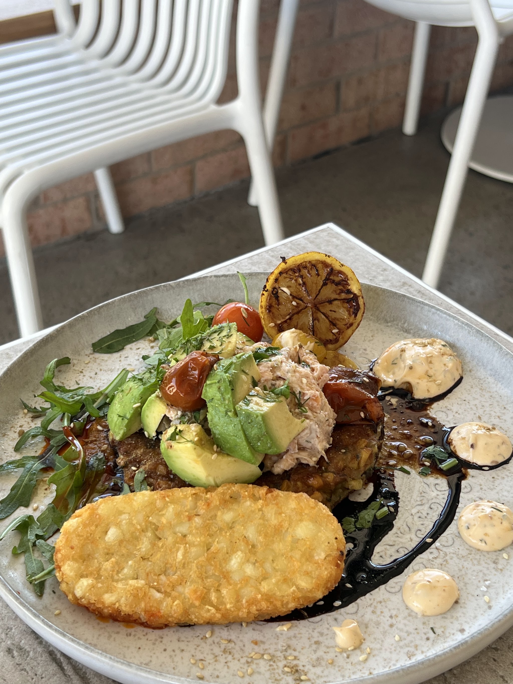 A stacked plate with avocado, cherry tomatoes, rocket, charred lemon and a hash brown