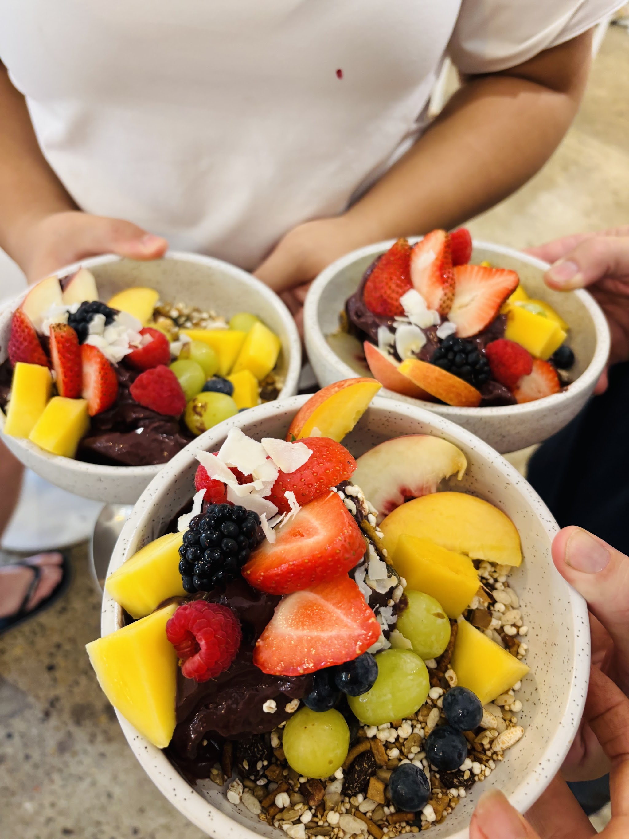 Three bowls piled with strawberries, mango, berries, grapes, coconut and granola