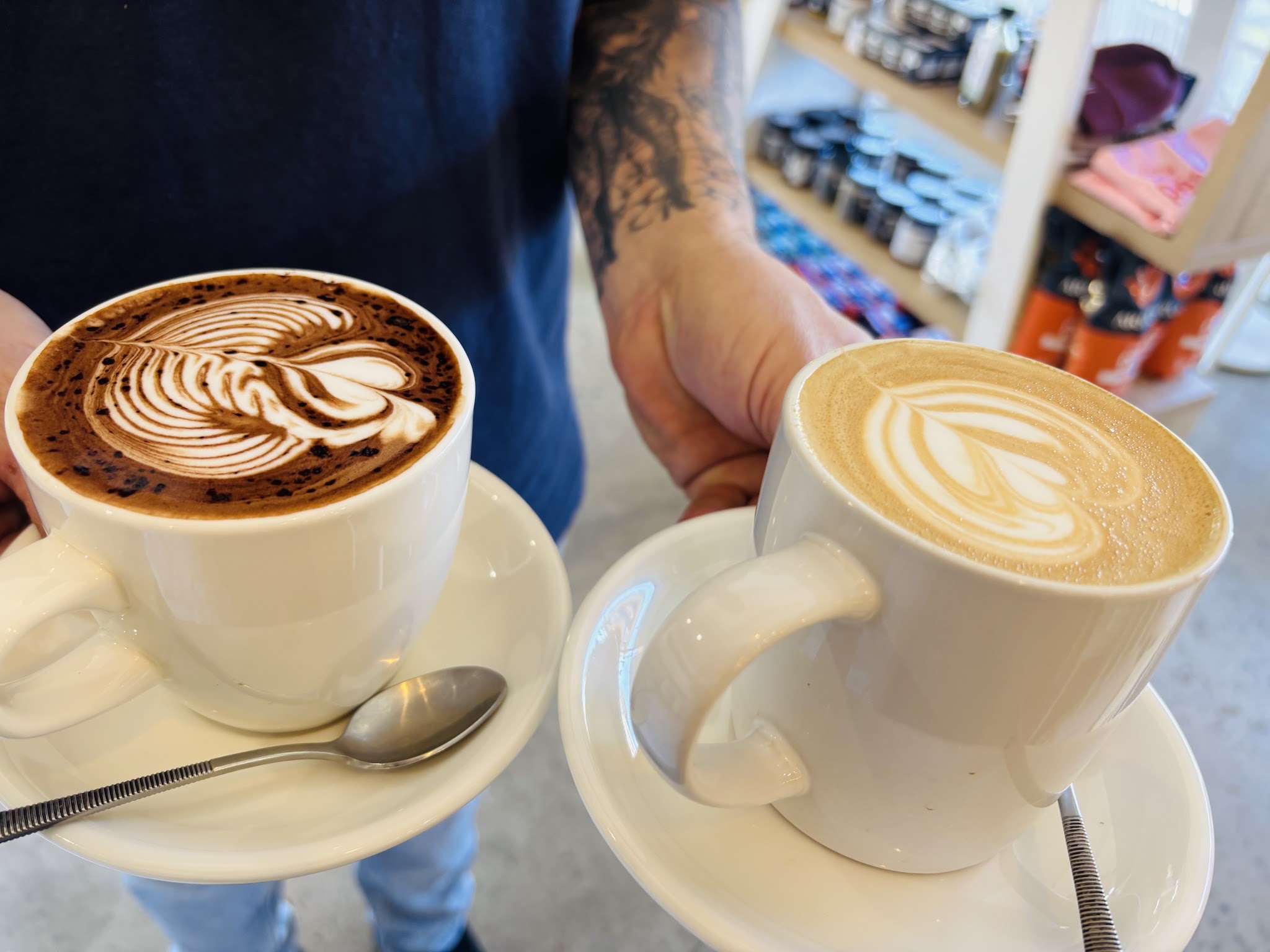 Two cups held up side by side, each topped with detailed rosetta latte art
