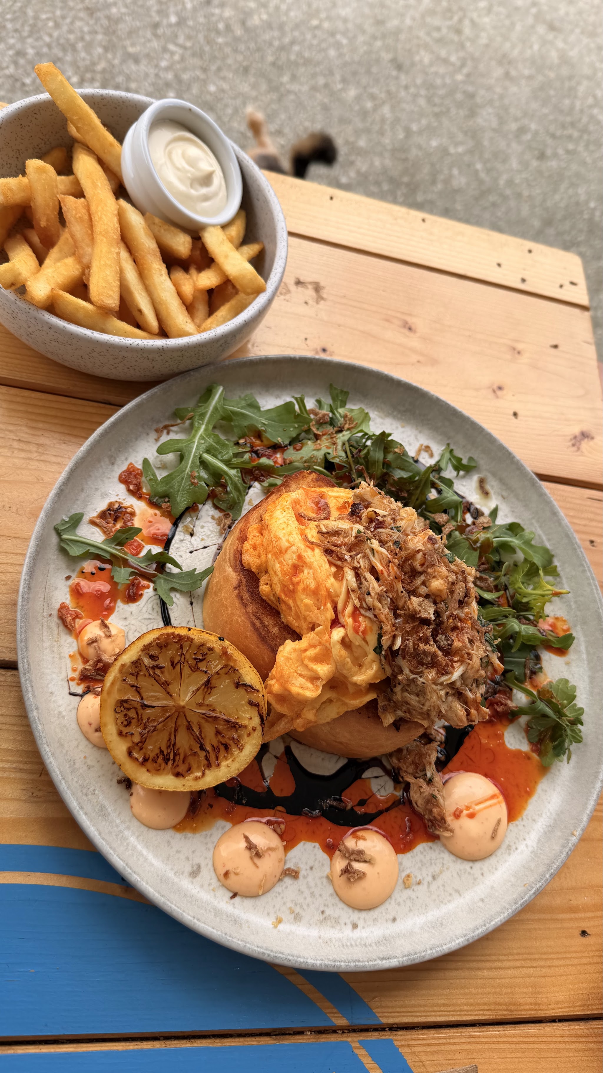A brioche bun with scrambled egg and shredded meat, rocket, charred lemon and a side of chips with aioli